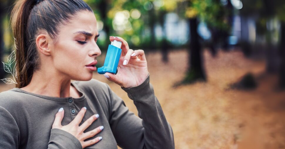 Mladá žena s tmavými vlasy držící modrý inhalátor a rukou na hrudi, v momentu dechové tísně – vizuál symbolizuje problémy s dýcháním.