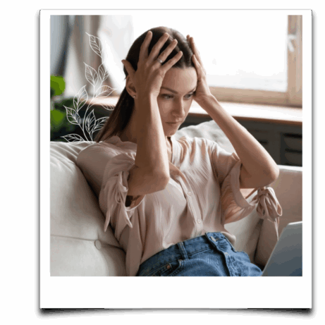 Mladá žena sedí na gauči s rukama ve vlasech a v napětí sleduje obrazovku notebooku – výrazně působí unaveně a přetíženě.