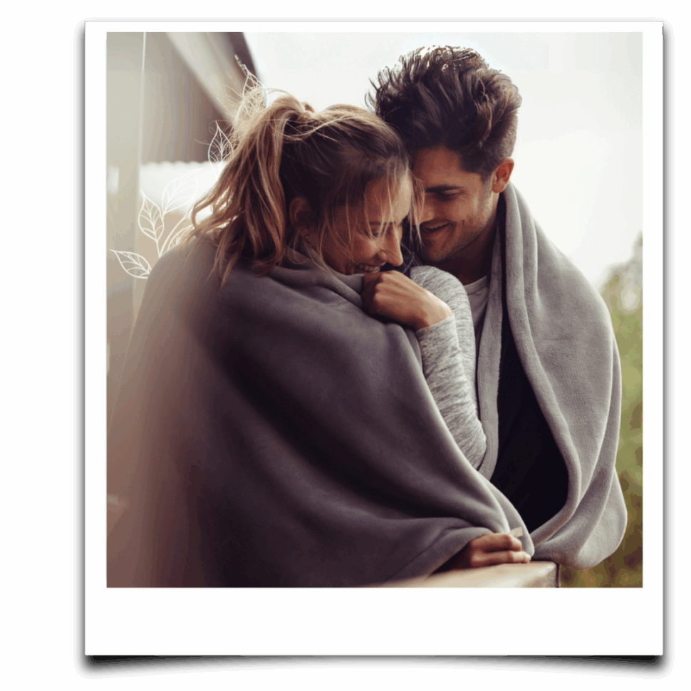 Mladý pár zabalený do deky na balkoně, v tichém a něžném objetí – obraz bezpečné intimity a klidného propojení.